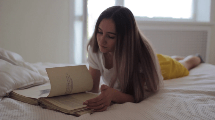 videoblocks-beautiful-girl-reading-a-book-in-bed-lying-on-her-stomach-smiling-happy-and-relaxed-on-a-leisure-day-at-home_hjrmutp8v7_thumbnail-full01